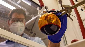 Camera angle looking up through a glass table where a person is using a pipette to drop drops in to a petri dish.