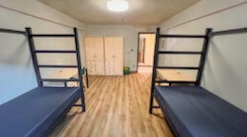 A room with two beds, two dressers, and two desks.