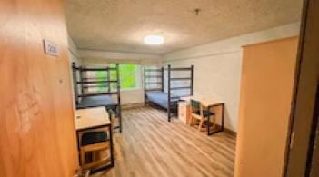 A room with two beds, two dressers, and two desks.