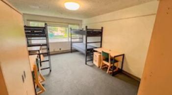 A room with three beds, three dressers, and two desks.