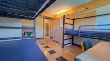 A room with three beds, three dressers/closets, three desks, and tile floors.