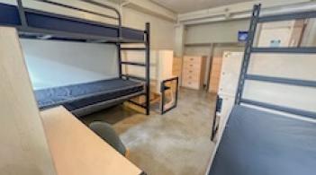 A room with three beds, three dressers, and three desks.