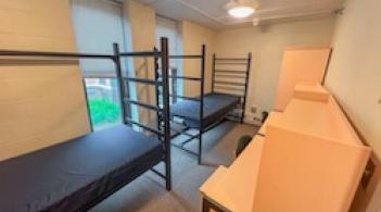 A room with two beds, two desks, and two dressers.