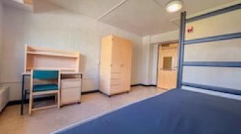 A room with one bed, one dresser/closet, and a desk.