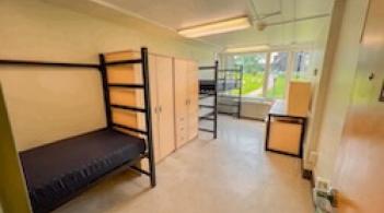 A room with two beds, two dressers, and two desks.