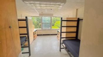 A room with two beds, two dressers, and two desks.