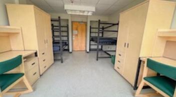 A room with two beds, two dressers, and two desks.