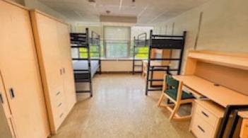 A room with three beds, three dressers, and three desks.