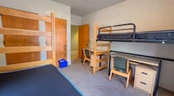 A room with two beds, two dressers/closets, and two desks.