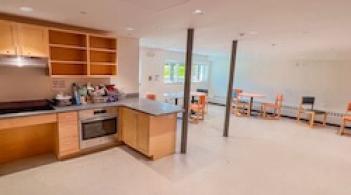 A kitchen and a large, brightly-lit dining area with several small tables.