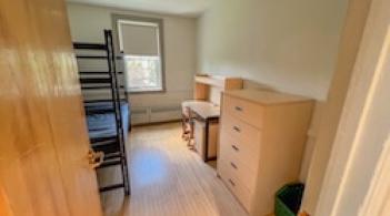 A room with wood floors and one bed, one dresser/closet, and a desk.
