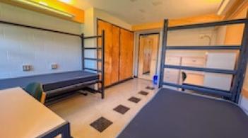 A room with two beds, two built-in closets, two desks, and tile floors.