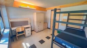 A room with a bed, desk, chair, closet/dresser, and tile floors.