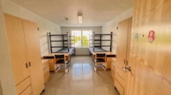 A room with two beds, two dressers/closets, and two desks.