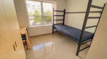 A room with one bed, one dresser/closet, and a desk.