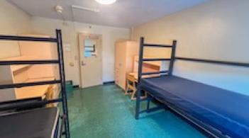 A room with two beds, two dressers, and two desks.