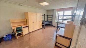 A room with two beds, two dressers, and two desks.