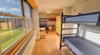 A room with a large window and three beds, three desks, and three closets.