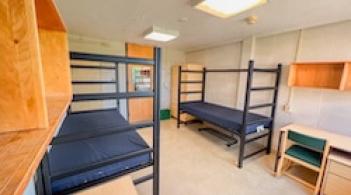 A room with two beds, two dressers, and two desks.