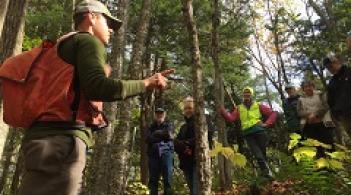 Alumni Ethan Tapper speaking with a group of people in the woods