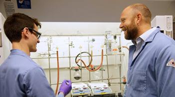 Two people wearing lab coats discussing research findings