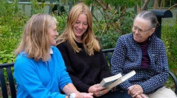 Two older woman and a female student looking at a book 