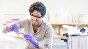 Student in a lab wearing goggles and gloves pouring liquid