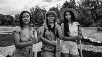 Black and white photograph of three women holding farm tools, Vermont landscape in the background.