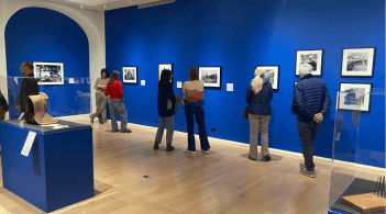 Groups of people looking at the hanged photographs in the gallery, the walls are bright blue.