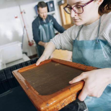 student holds a tray above chemicals with a professor in background