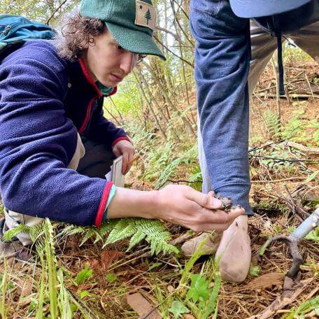 two students inspect a soil sample in the forest