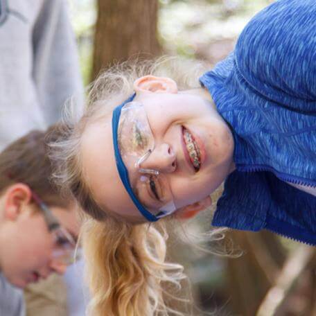 young girl tilted sideways wearing goggles and smiling