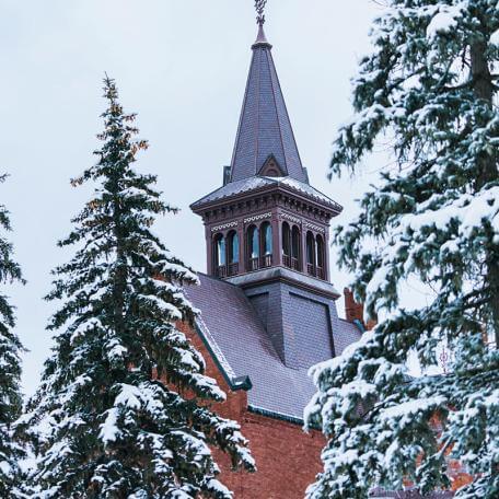 snow on pine trees in front of old mill tower