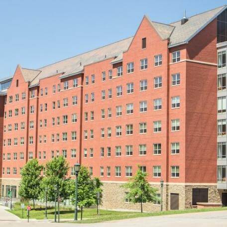 A seven-story, brick residence hall with trees and grass in the foreground.