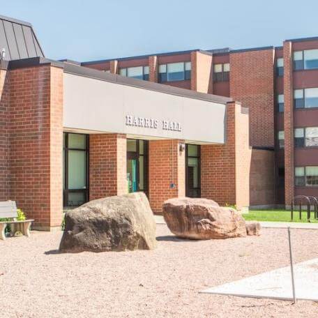 A 3-story brick residence hall with a grassy area and trees surrounding it. 