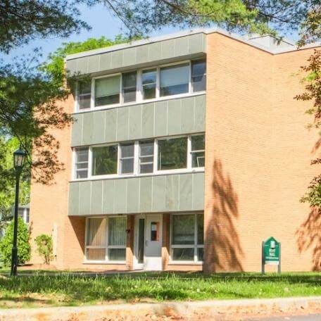 A 3-story brick residence hall with a grassy area and trees surrounding it. 