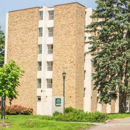 A 6-story stone and concrete building with trees and grass in the front.