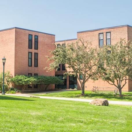 A 3-story brick residence hall with a grassy area and trees surrounding it. 