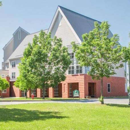 Modern, three-story residence hall with trees and grassy area. 