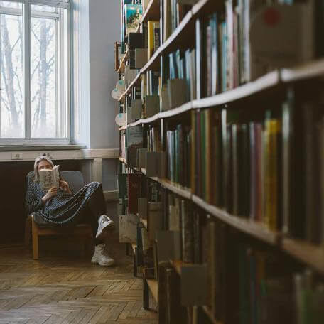 filled bookshelves and a woman sitting in the background reading