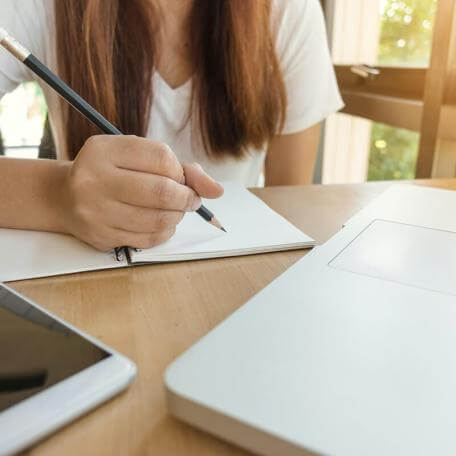 student at a desk with pencil and notebook and a laptop