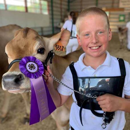 smiling kid with his cow sporting a purple victory ribbon
