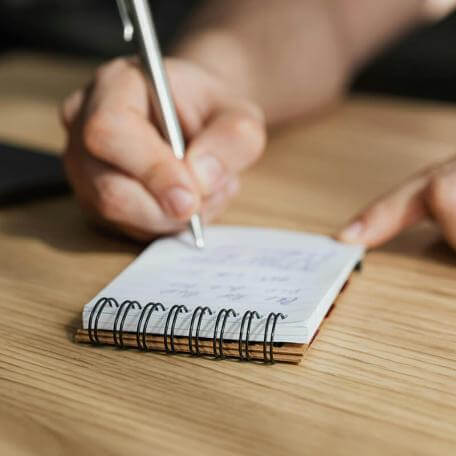 close up of a hand writing with a pen on a small pad of paper