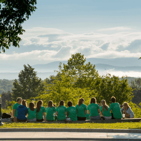 Students sitting in a group outside on the grace with mountains and trees in the background