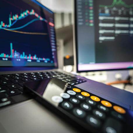 a calculator next to two computer monitors with financial information on them