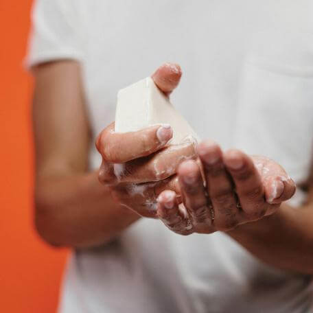 closeup of someone in a t-shirt washing their hands with a bar of soap