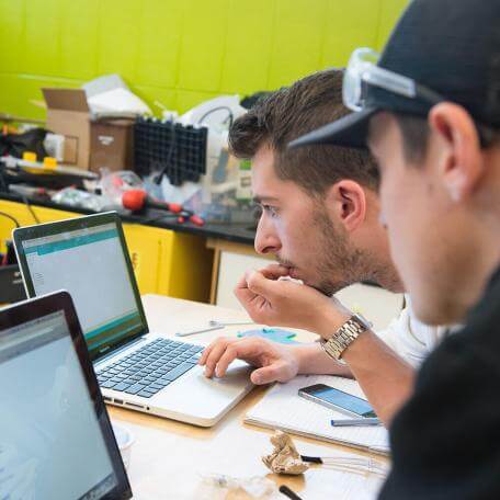 Two students working on laptops, collaborating on a project