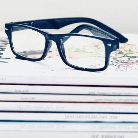 a stack of magazines with a pair of glasses on top of them