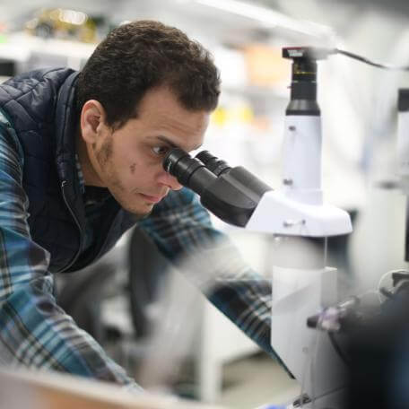 Scientist looking into a microscope in a lab, links to Past Research Projects Page 