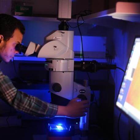 person in dark lab looking into a massive microscope